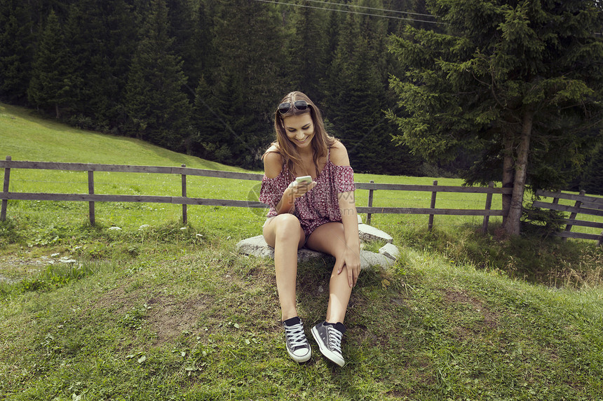 奥地利蒂罗尔Sattelbergalm坐在田野里阅读智能手机短信的年轻女子图片