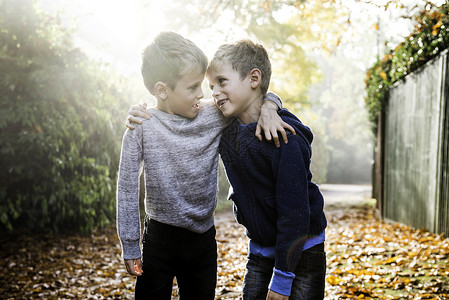 孪生兄弟双胞胎男孩的肖像户外面对被秋叶环绕的背景