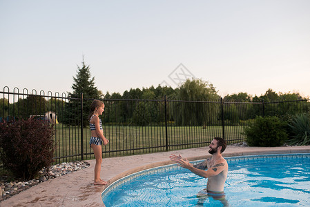 站在游泳池边缘的年轻女孩父亲在游泳池鼓励她跳进游泳池图片