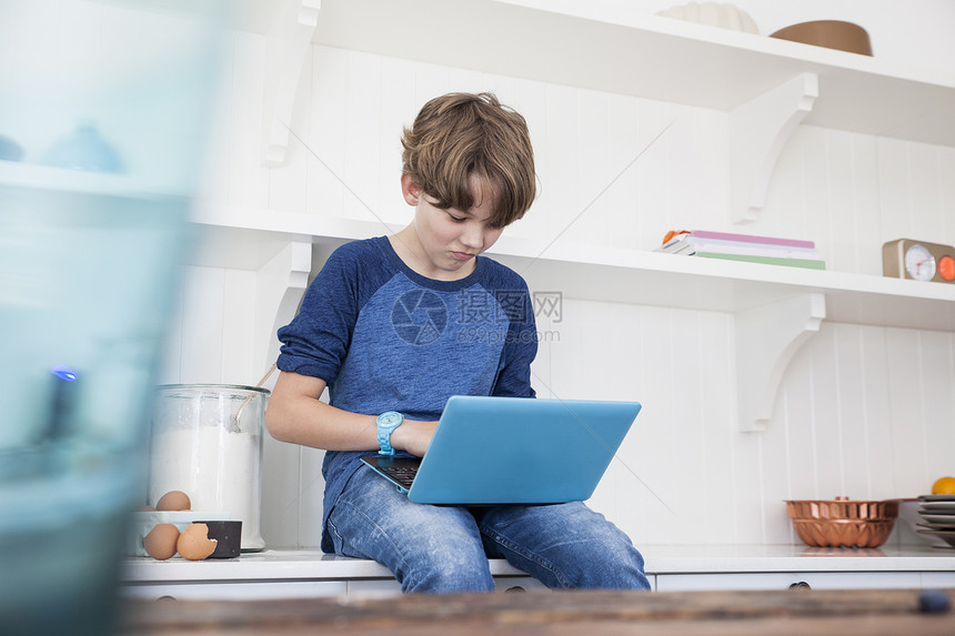 男孩坐在厨房工作表面使用膝上型电脑图片