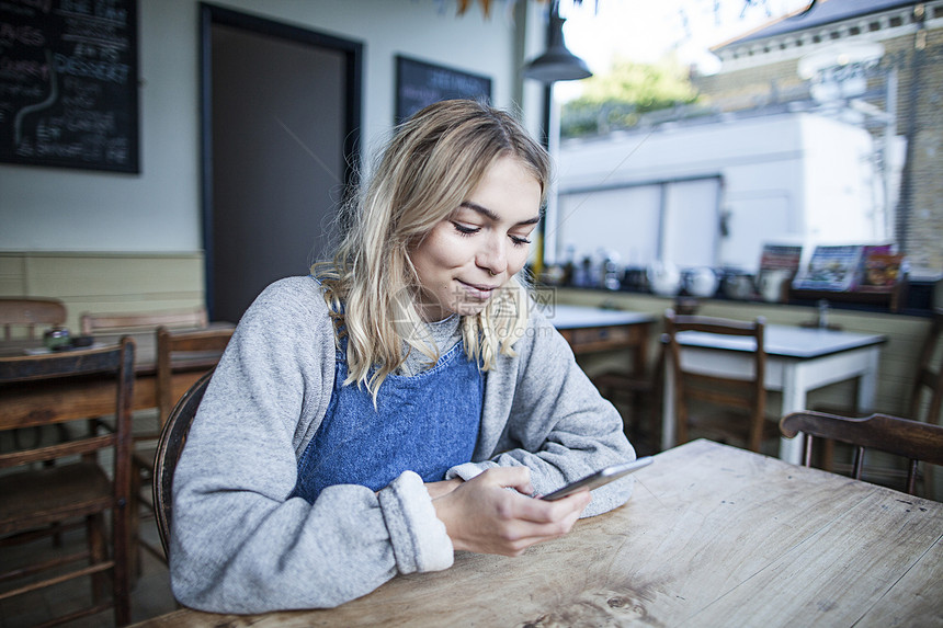 坐在咖啡馆的年轻女子使用智能手机微笑图片