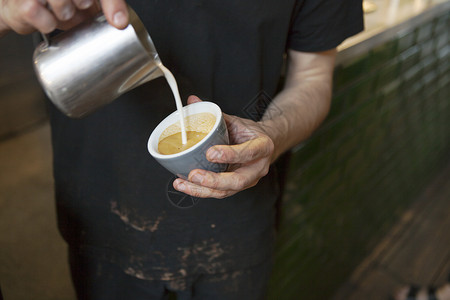 咖啡馆男咖啡师用手往咖啡杯里倒牛奶图片