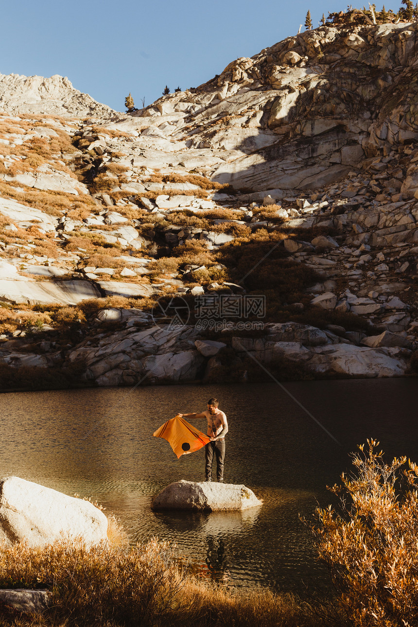 美国加利福尼亚州红杉公园带着毛巾站在湖中岩石上的年轻男徒步旅行者图片