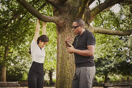 个人教练指导妇女使用公园树枝进行引体向上图片