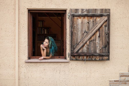 蓝头发的年轻女人看着窗外的图片