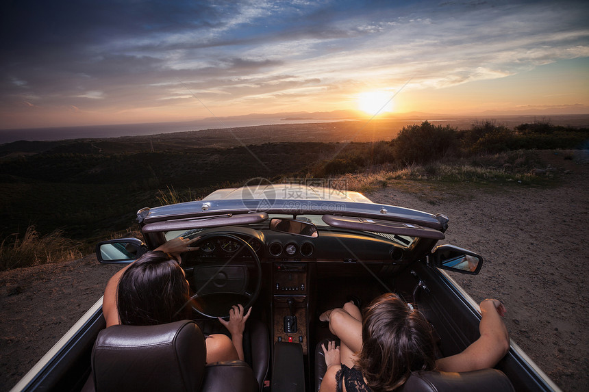 2名青年妇女乘坐敞篷车沿风景路后视行驶图片