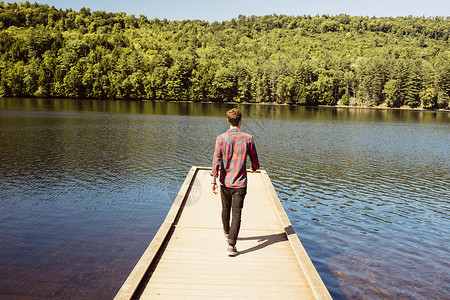 男人在湖边的木码头上行走后视图片