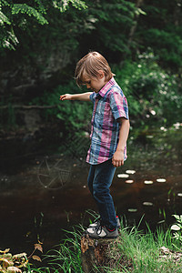 男孩在河岸的树桩上保持平衡图片