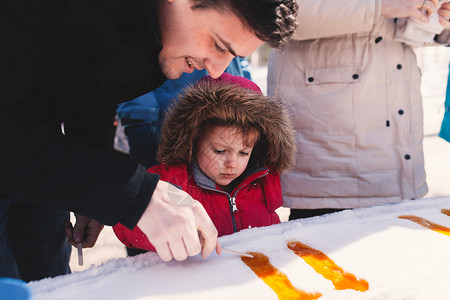 穿着毛皮兜帽的女孩跟父亲在雪中做甜食图片
