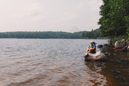 男孩坐在湖边的岩石上图片