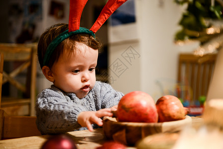 盯着桌上石榴的戴着圣诞鹿角的小男孩图片