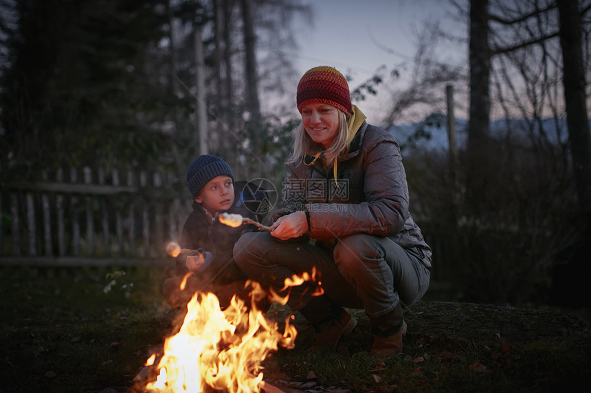 成年女人和儿子在黄昏的花园营火上烤棉花糖图片