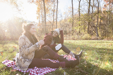 坐在野餐毯子上笑着的两名年轻妇女高清图片