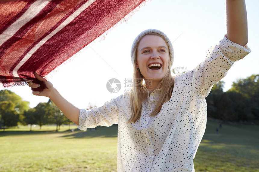 在公园里大笑着摇野餐毯子的年轻女人图片