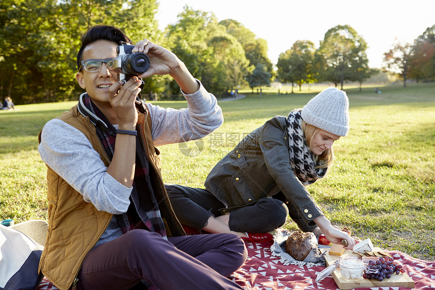 在公园女朋友在拿野餐食物男人在拍照图片