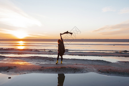 妇女日落时在海滩挥舞围巾图片