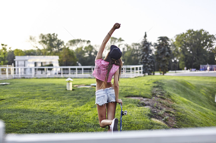 年轻妇女在公园中拿着滑板打气后视图片