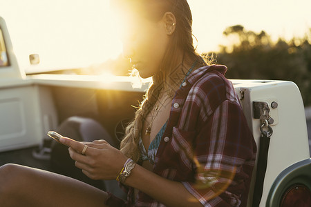 坐在皮卡车上的青年女性看智能手机图片