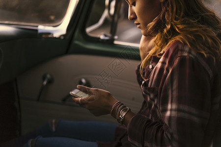 坐在皮卡车里看智能手机的年轻女子图片
