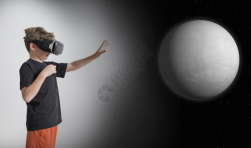 男孩佩戴虚拟现实头盔伸手触摸数字合成的行星图片