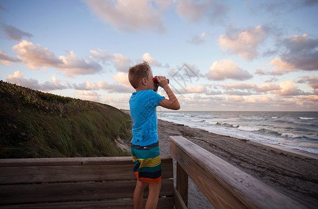 男孩在海滩通过望远镜看风景吹落岩保护区木星佛罗里达州美国图片