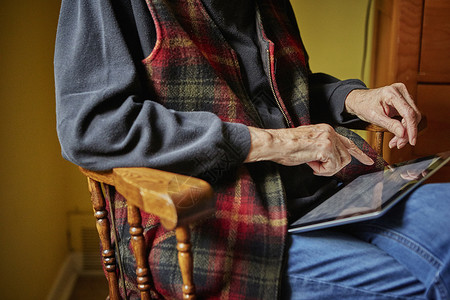 老年妇女坐在椅子上用平板电脑图片