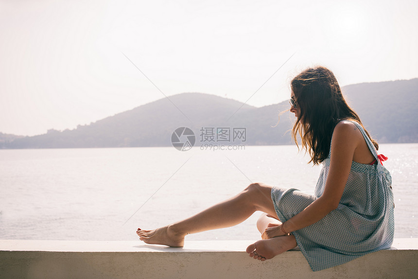 海上坐在墙的年轻妇女图片