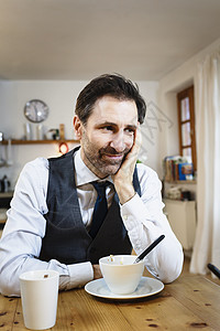 在厨房吃早餐时用手托着下巴笑的成年男子图片