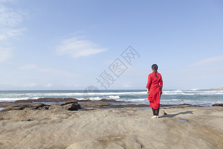 身着红裙子站在岩石上看着海景的妇女南非图片