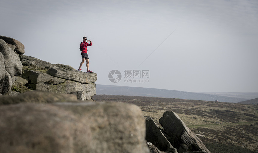 英国德尔比郡峰地区岩石顶部拍摄照片的男性图片