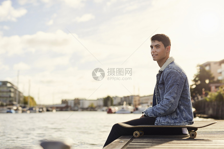 坐在河边滑板旁的年轻人英国布里斯托尔图片