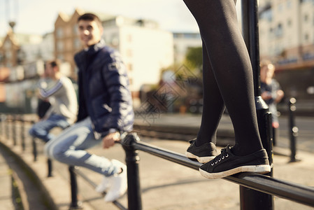坐在栏杆上的年轻男子看着女孩在他旁边的栏杆上行走英国布里斯托尔图片