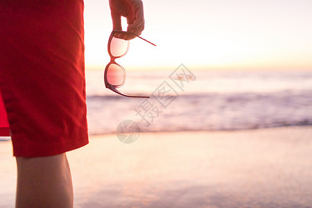 日落时分在沙滩上拿着太阳眼镜的妇女图片