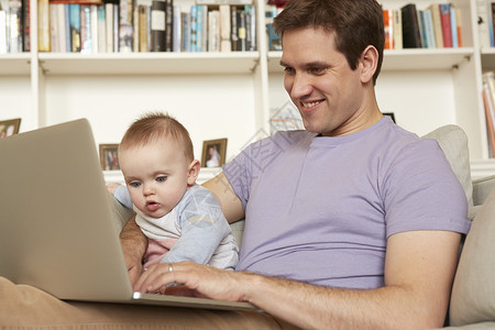 婴儿女孩看父亲在沙发上打笔记本电脑图片