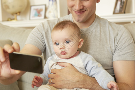 中年男子在沙发上用智能手机自拍和女儿婴在沙发上图片