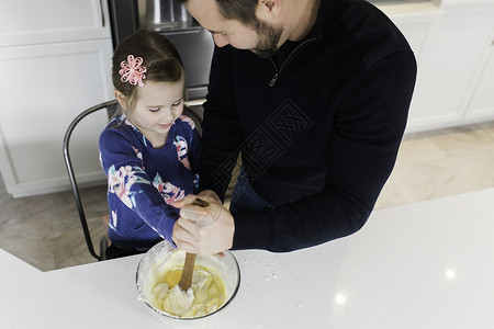 成年男子和女儿在厨房柜台一起搅拌食材图片