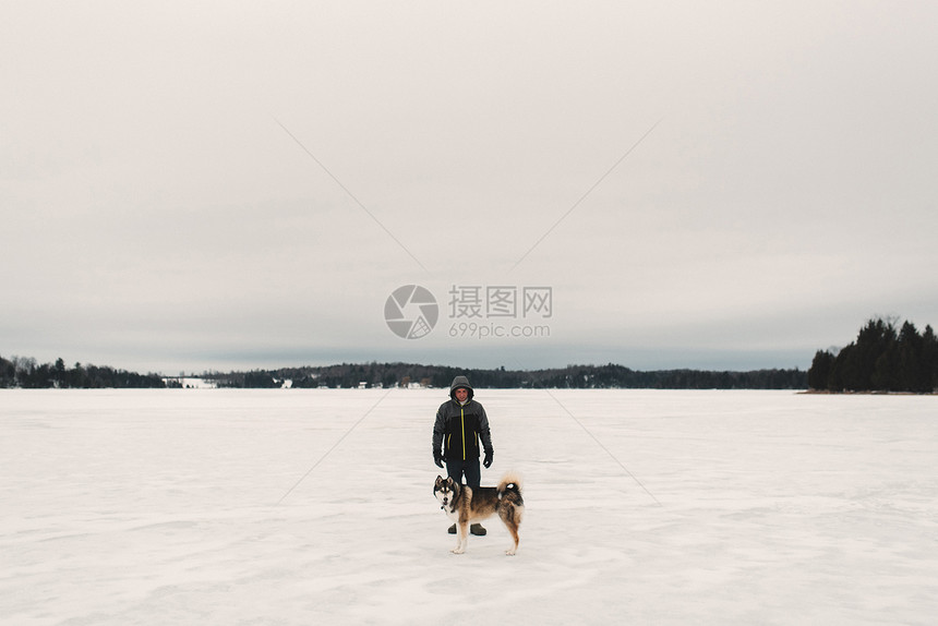 在雪覆盖的风景中与霍斯基狗站在一起的人肖像图片