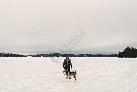 在雪覆盖的风景中与霍斯基狗站在一起的人肖像图片