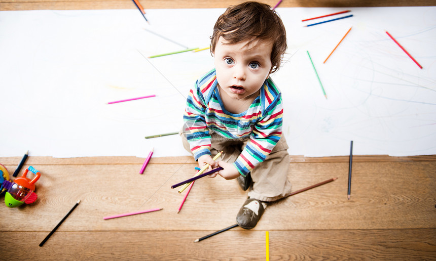 用彩色铅笔和长纸坐在地板上的男幼儿头部视线图片