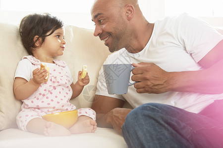 女孩和父亲坐在沙发上吃零食图片