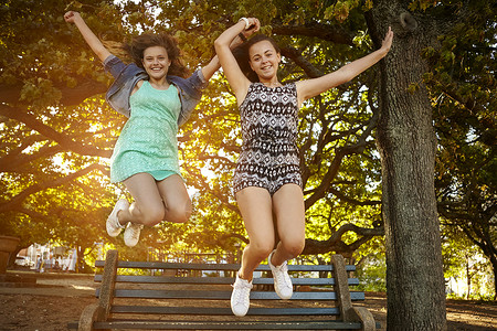 两名女朋友跳下公园长凳的肖像图片