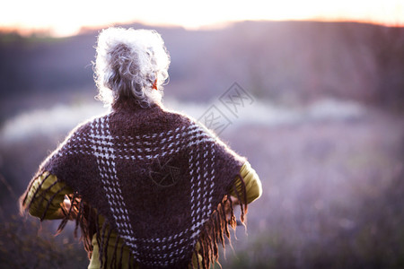 白头发老奶奶手叉腰看日落的背影高清图片