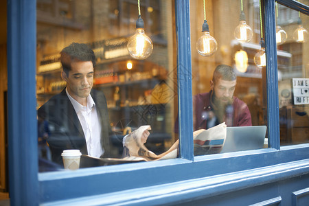商人阅读报纸和使用咖啡馆笔记本电脑的视窗图片