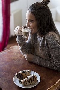 坐在桌边的年轻女人喝咖啡吃糕点图片