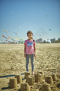 年轻女孩站在沙滩城堡后面意大利图片