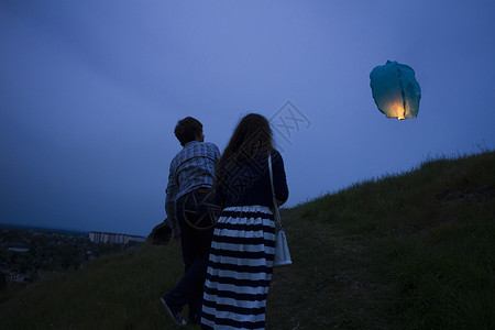 万人天灯一对夫妇在黄昏时草地上行走看着空中的天灯背景