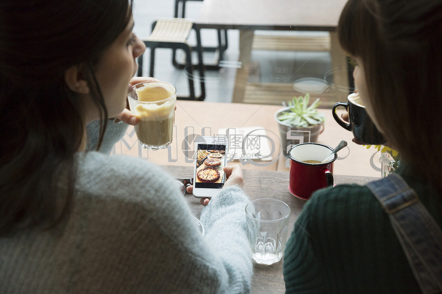 坐在咖啡馆的两名年轻妇女看着手机上的照片图片
