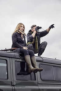 来狩猎的夫妻在车顶上拿着望远镜向远看图片