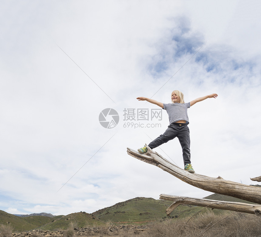 在树干尾端保持平衡张开手臂的男孩图片