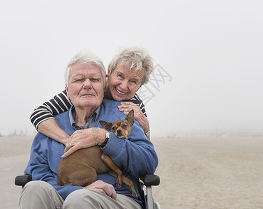 海滩上的妻子和抱着狗坐在轮椅的老人图片
